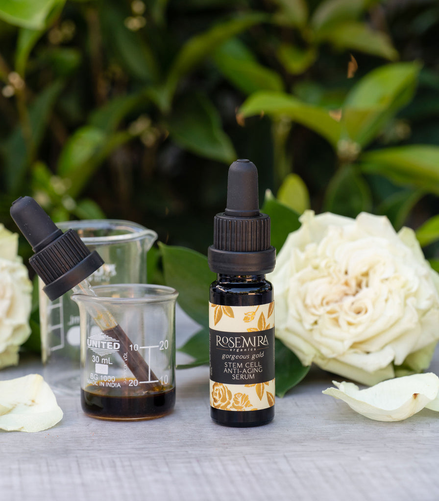 Gorgeous Gold Stem Cell Anti-Aging Serum with a beaker of dark gold serum and white roses.