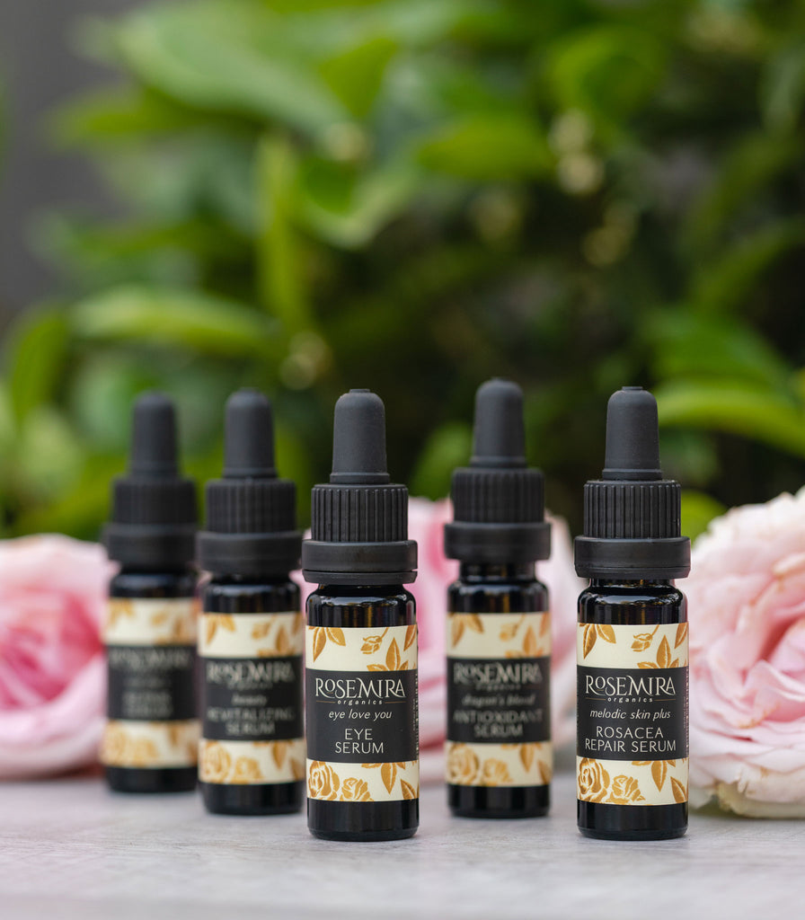 A row of five organic serums in black bottles with pink roses.