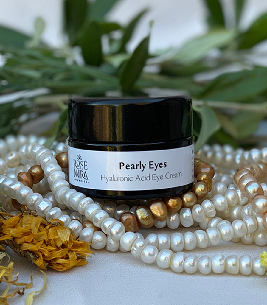 A black bottle of eye cream placed on freshwater pearls with green leaves