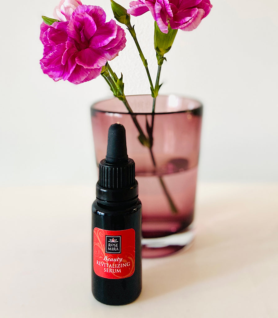 Beauty Revitalizing Serum with a pink carnation in a glass.