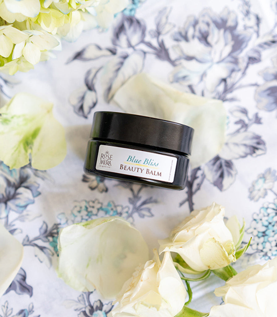 Blue Bliss Beauty Balm with white rose petals on a flower tablecloth.
