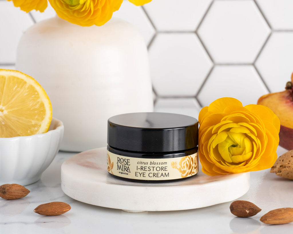 Citrus Blossom I-Restore Eye Cream with yellow flowers, lemons, and almonds on marble.