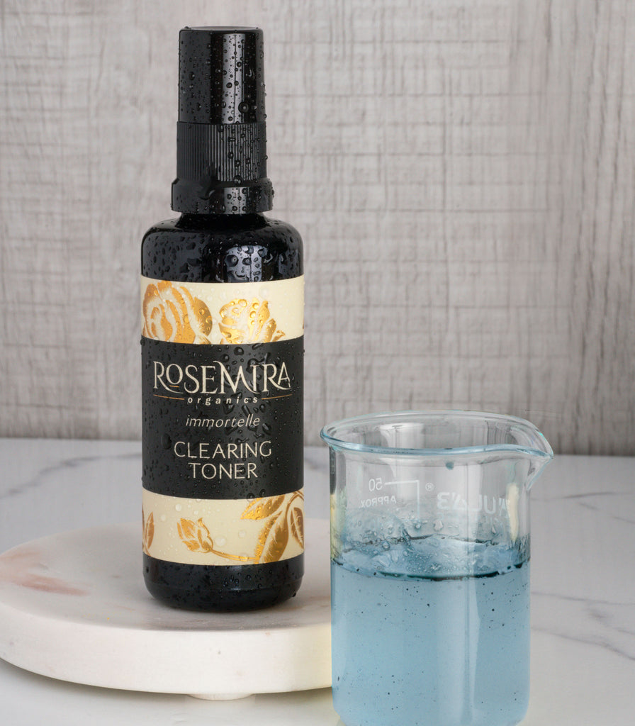 Immortelle Clearing Toner on a white marble tray with a beaker of blue tansy.