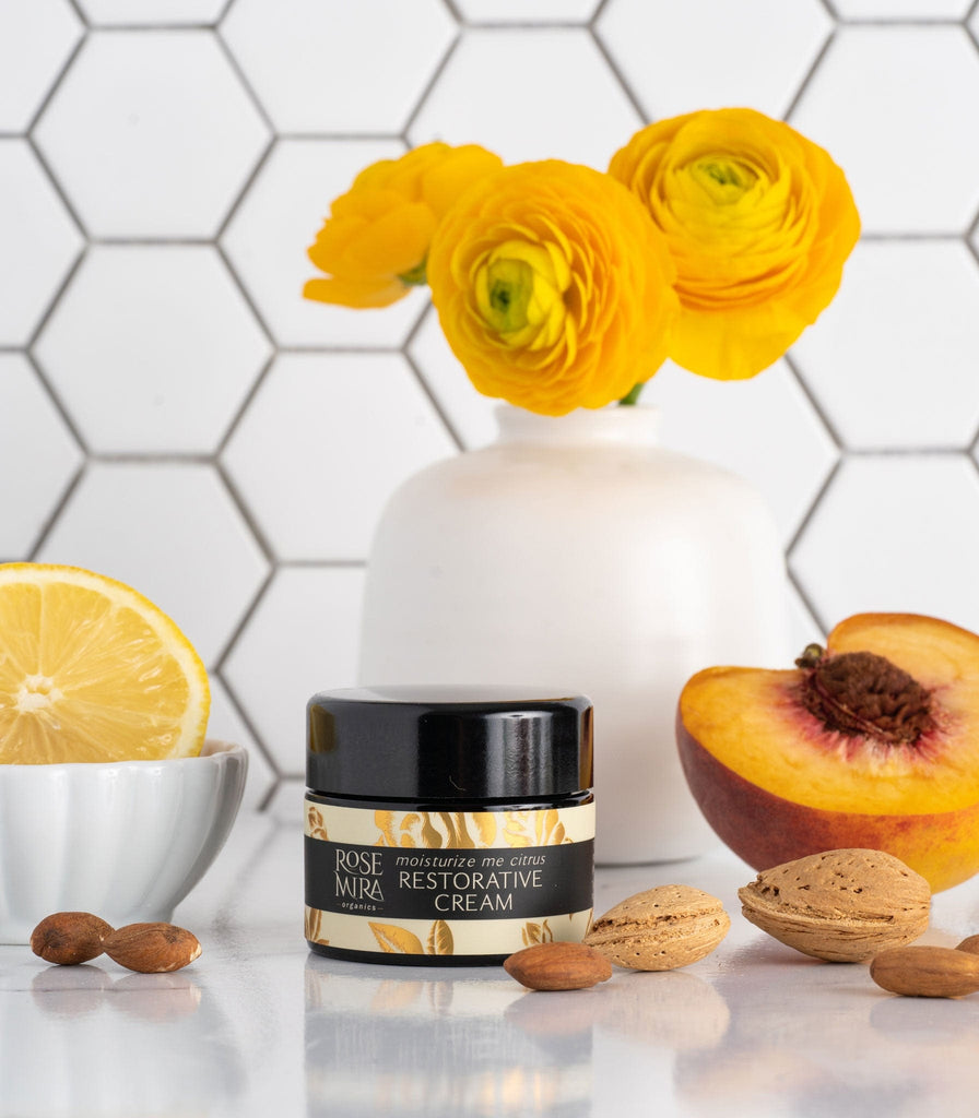 Moisturize Me Citrus Face Cream with almonds, lemon, peach, bouquet of yellow flowers on white table.