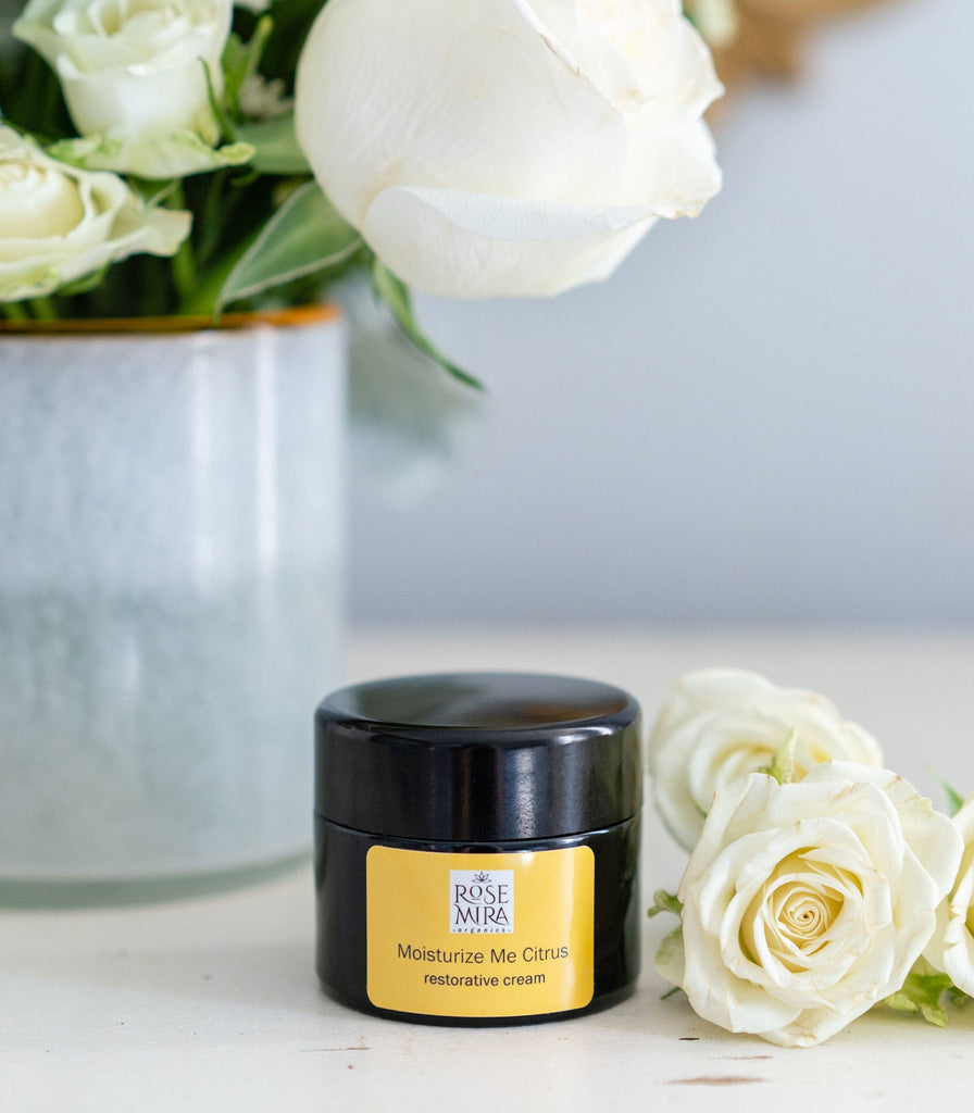 Moisturize Me Citrus Restorative Cream with white roses and a gray ceramic vase.