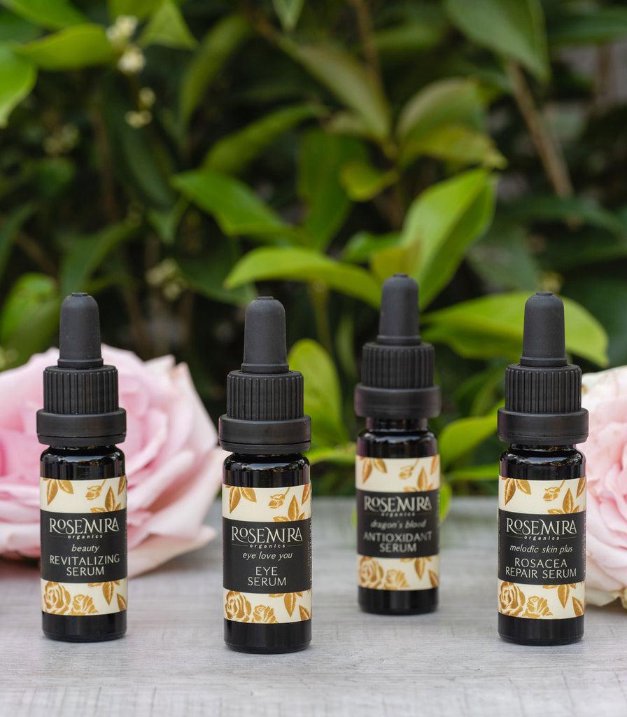 A row of four organic serums in black bottles with pink roses.