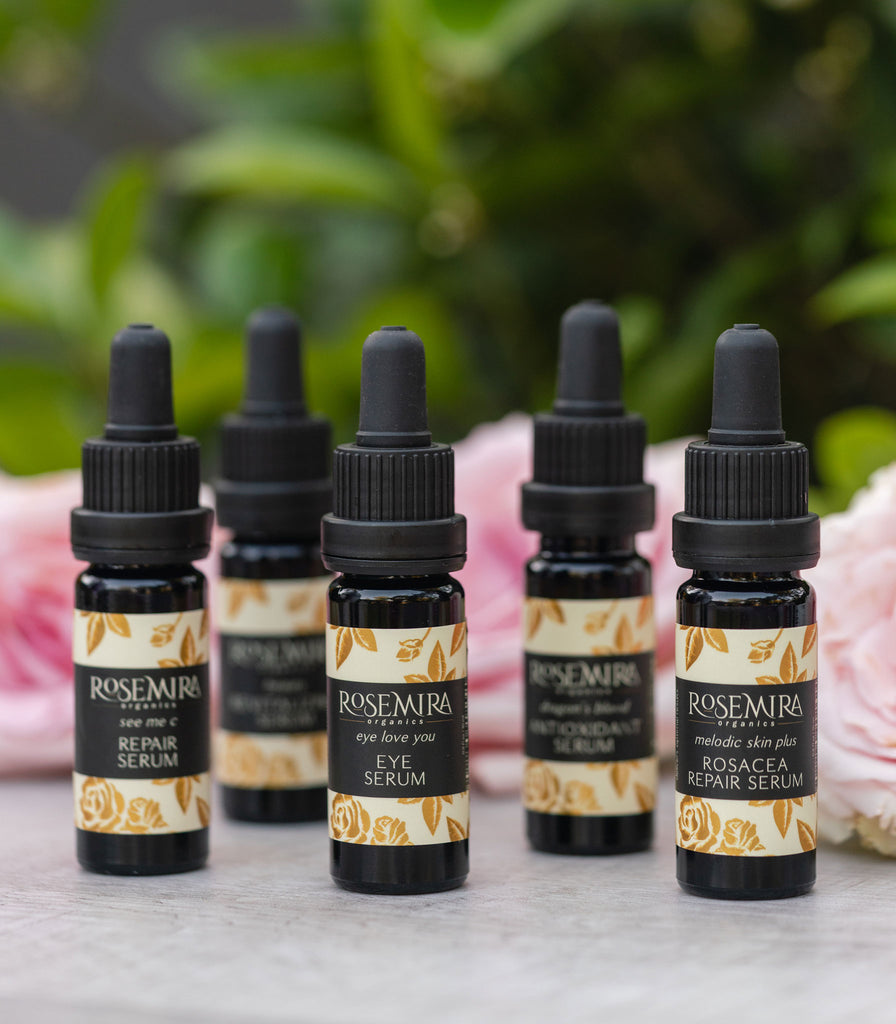 A row of five organic serums in black bottles with pink roses.